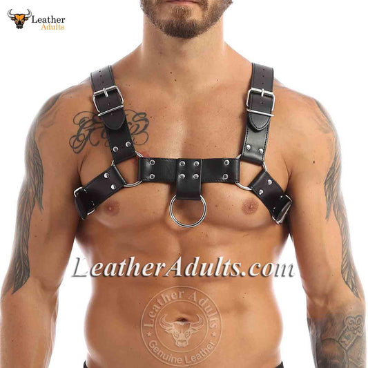 A man wearing a black leather chest harness with stainless steel hardware, featuring adjustable buckles and a ring attachment at the front.