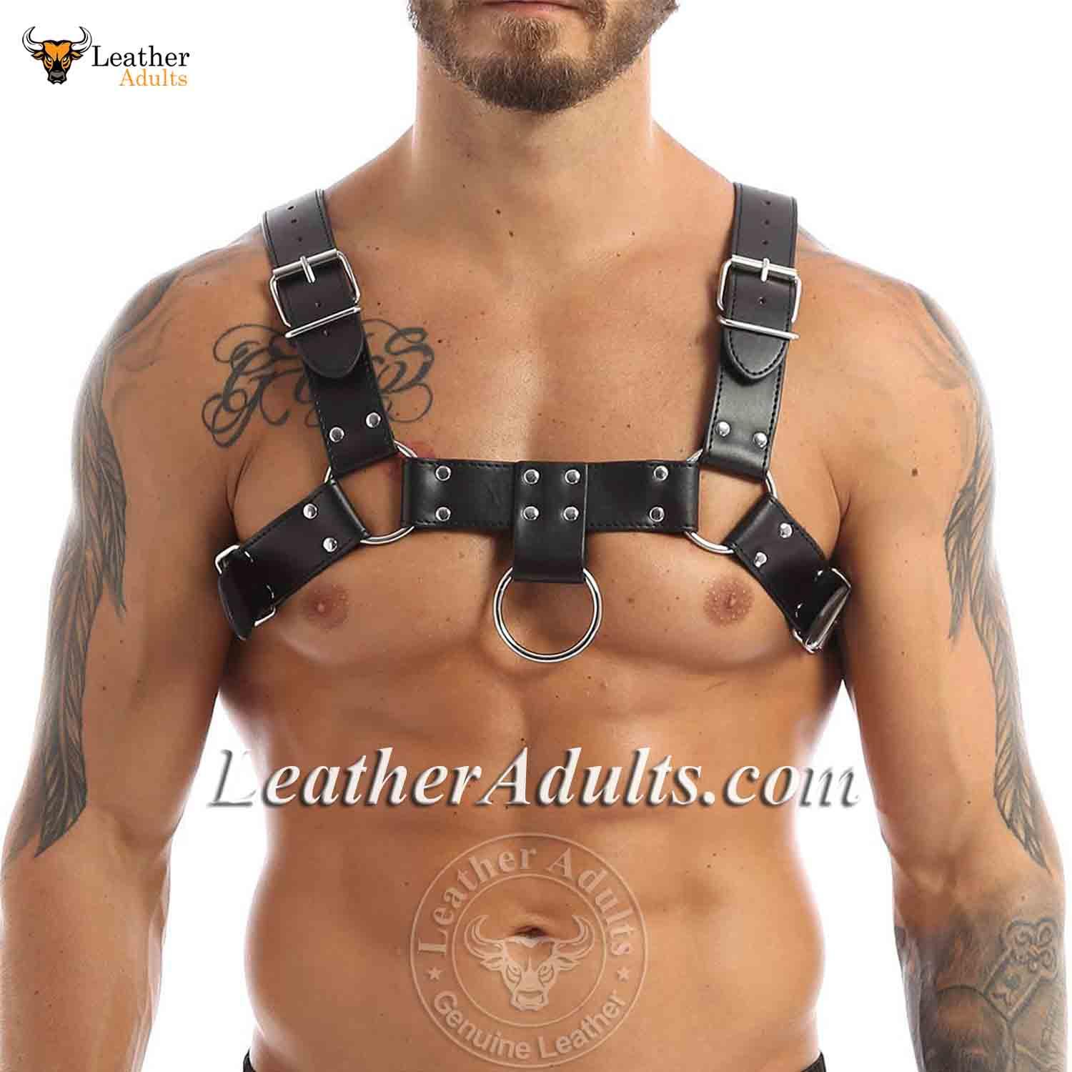 Man wearing a black leather harness with visible tattoos on a white background, featuring 'LeatherAdults.com' branding.