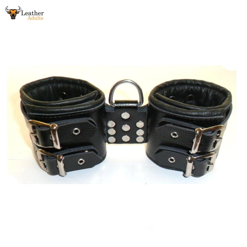 A pair of black leather wrist cuffs with metal buckles and a welded D-ring in the center.