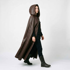 Side profile walking view of woman wearing full length brown leather fantasy cape with deep attached cowl hood and leather boots