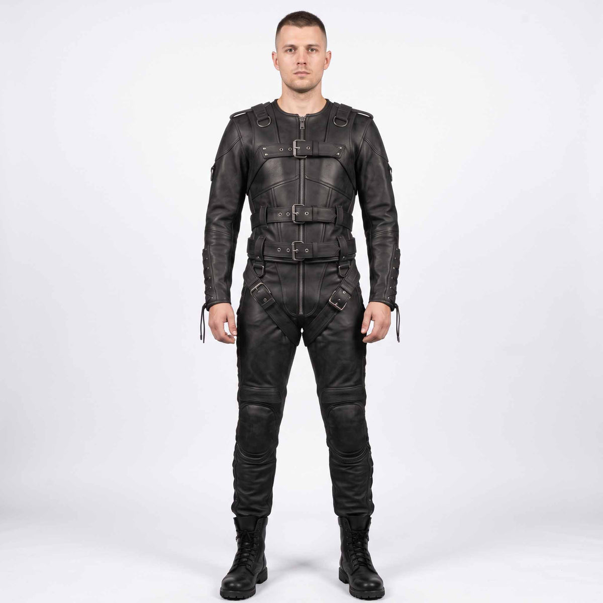 Full length front view of athletic man wearing handmade black cowhide leather restraint suit with front buckle straps, padded knees, and combat boots