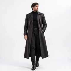 Full length front view of handsome man walking in handmade black genuine leather long trench coat open over dark turtleneck and trousers
