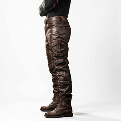 Side profile view of mens tailored brown leather biker trousers showing multi-tier buckle straps along thigh and calf stacked over lace up boots