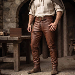 Front view of man standing in medieval workshop wearing handmade brown cowhide leather pants with front lace up fly and leather belt