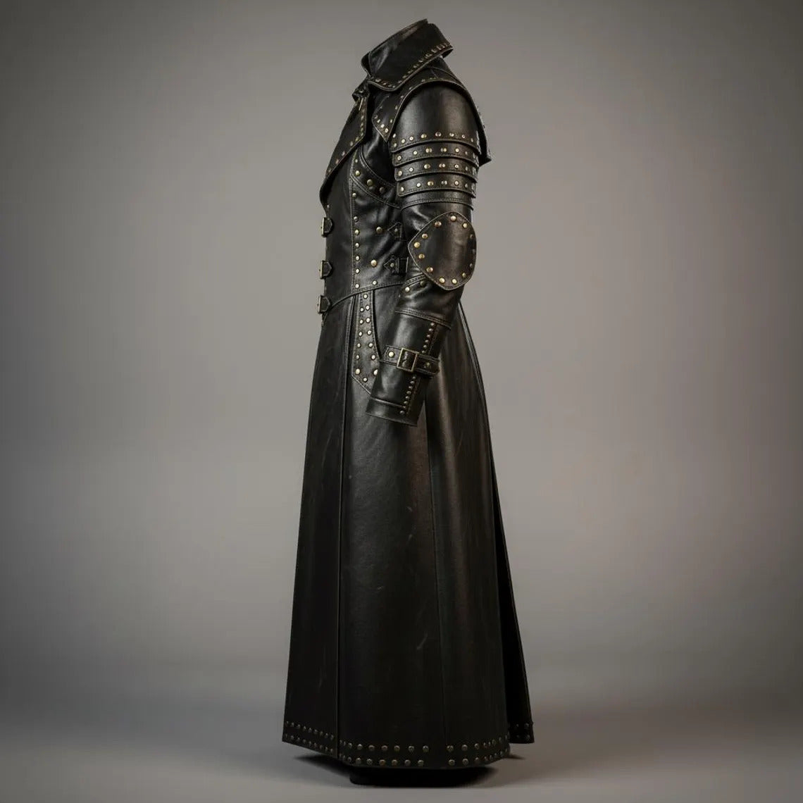 Side profile angle of mens black leather duster coat detailing studded elbow guards, tiered shoulder plates, and gauntlet cuff buckle straps
