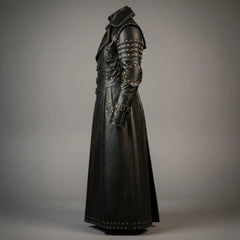 Side profile angle of mens black leather duster coat detailing studded elbow guards, tiered shoulder plates, and gauntlet cuff buckle straps