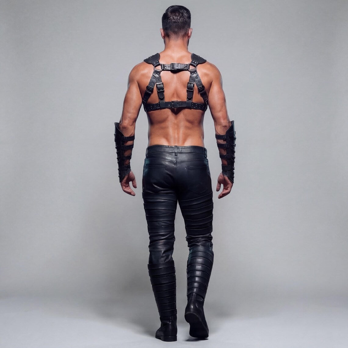 Rear view of man walking away in black genuine leather chest harness and tailored leather pants showing back buckle straps and clean rear pockets