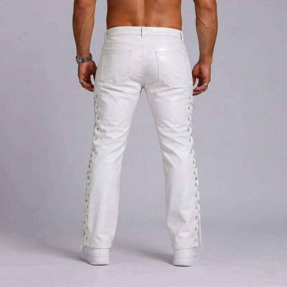 Back view of male model wearing white real cowhide leather pants showing the rear patch pockets and side lace-up seams down the legs.