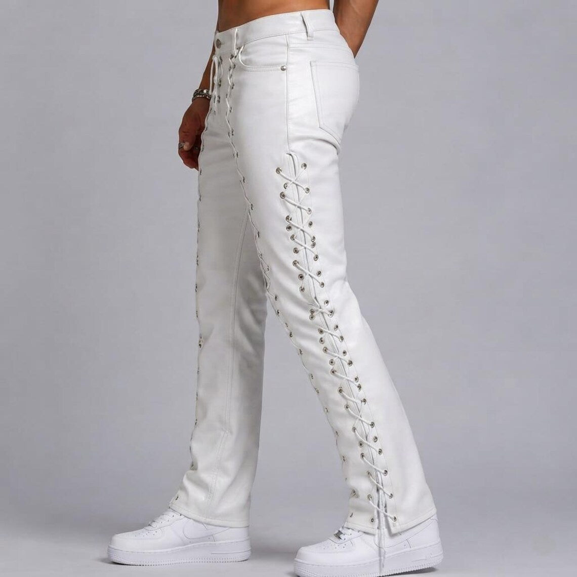 Side profile view showcasing the silver eyelets and full-length crisscross lace-up detail along the outer seam of men's white leather biker pants.