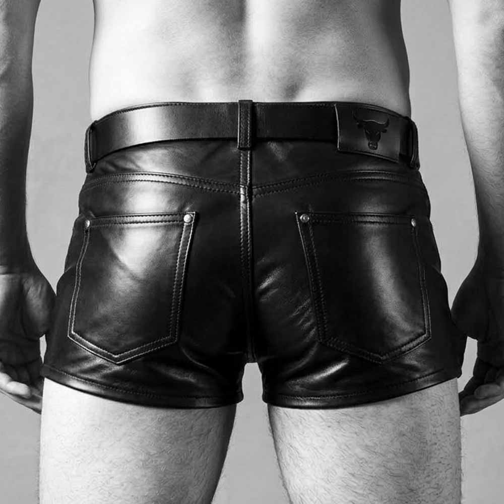 Back view of men's fitted black real leather shorts displaying riveted rear patch pockets, embossed leather waist patch, and belted waist.