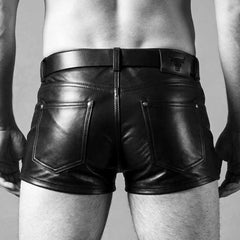Back view of men's fitted black real leather shorts displaying riveted rear patch pockets, embossed leather waist patch, and belted waist.