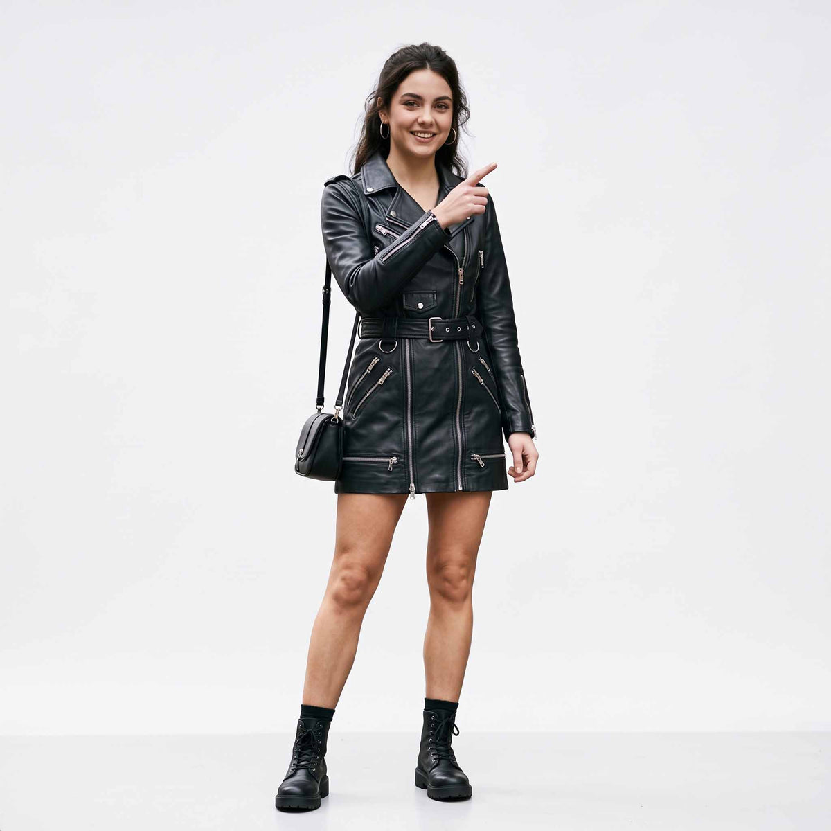 Full length view of woman wearing handmade black leather mini dress with belt, asymmetric zipper, and black combat boots pointing forward