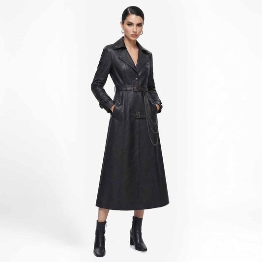 Front view of a woman wearing a long black leather trench coat with a belted waist and hanging chain detail, paired with heeled boots.