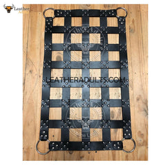 A black leather cargo swing sling with stirrups, featuring a grid-like pattern and branded with the text 'LEATHERADULTS.COM'.